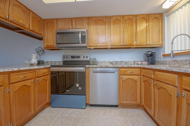 kitchen with light tile patterned floors, brown cabinetry, a sink, light countertops, and appliances with stainless steel finishes