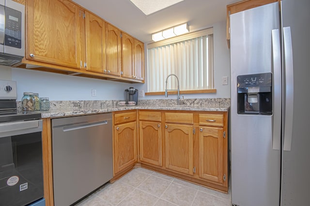 kitchen with light tile patterned flooring, light stone countertops, appliances with stainless steel finishes, and a sink