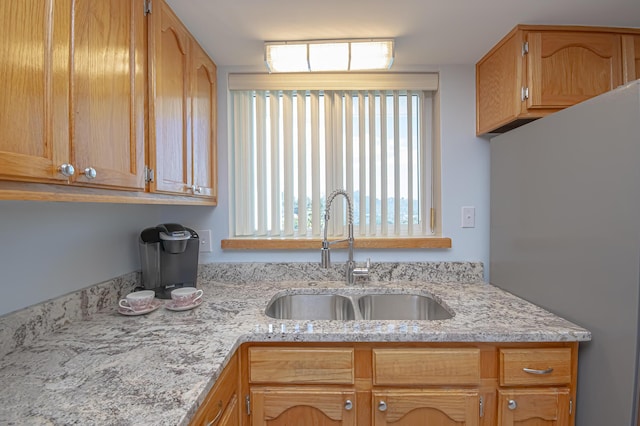 kitchen featuring light stone counters, freestanding refrigerator, and a sink