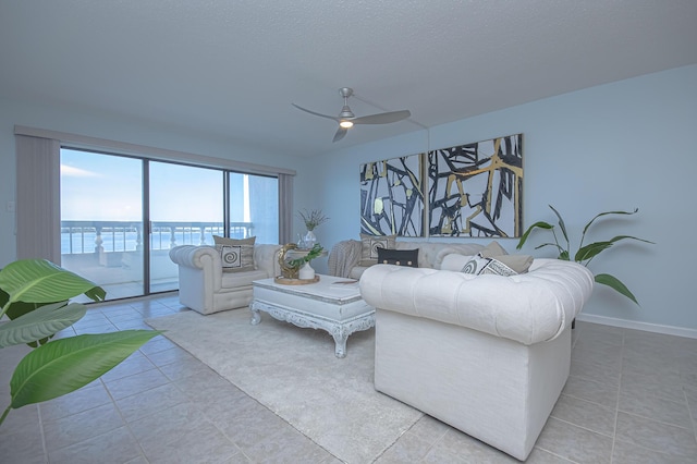 living area featuring tile patterned floors, a ceiling fan, baseboards, and a textured ceiling