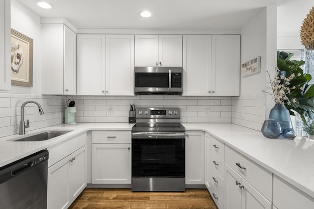 kitchen featuring white cabinets, backsplash, light hardwood / wood-style flooring, appliances with stainless steel finishes, and sink