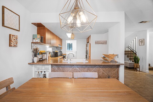 kitchen with stainless steel refrigerator, sink, an inviting chandelier, tile patterned flooring, and pendant lighting