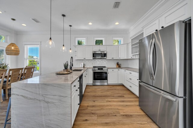 kitchen with appliances with stainless steel finishes, light stone counters, white cabinetry, sink, and pendant lighting