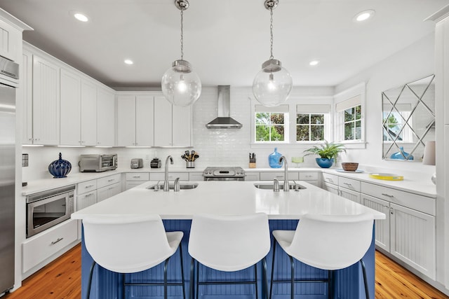 kitchen with an island with sink, stainless steel appliances, sink, and wall chimney exhaust hood