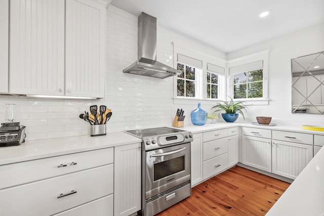 kitchen with white cabinets, stainless steel range with electric cooktop, light hardwood / wood-style flooring, wall chimney range hood, and tasteful backsplash