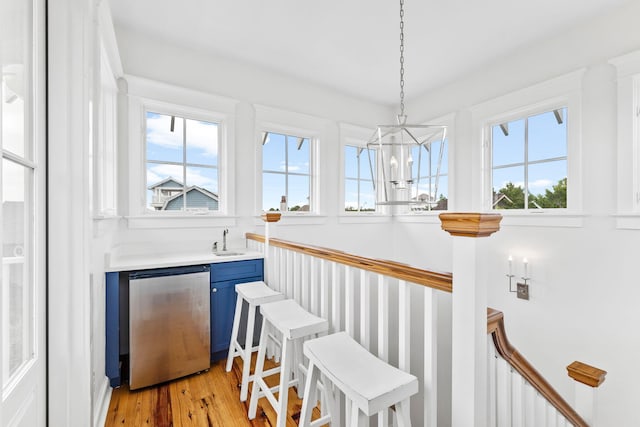 bar with pendant lighting, light hardwood / wood-style flooring, sink, blue cabinets, and stainless steel dishwasher