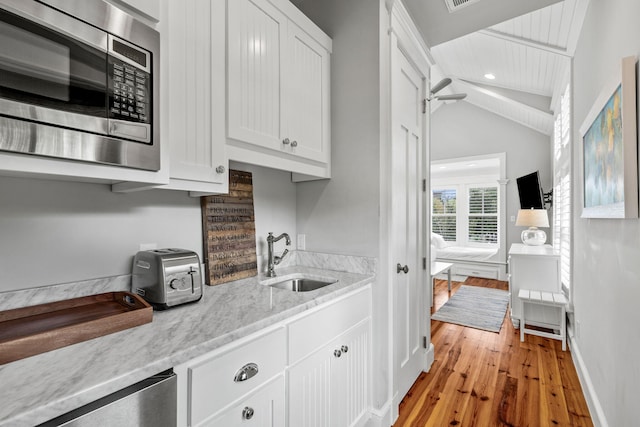 kitchen with light wood-type flooring, white cabinetry, sink, stainless steel microwave, and lofted ceiling