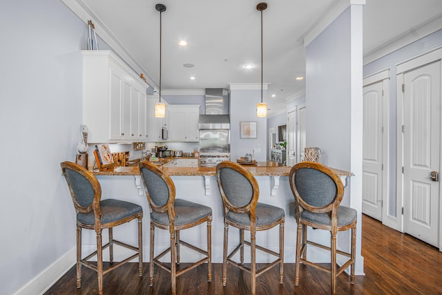 kitchen featuring light stone counters, white cabinetry, wall chimney exhaust hood, kitchen peninsula, and pendant lighting