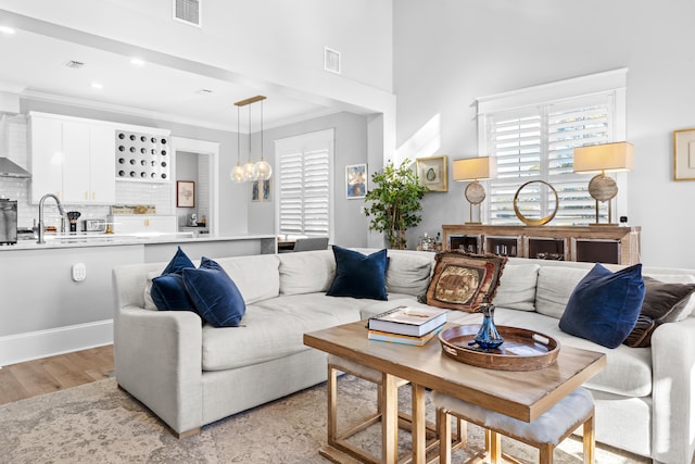 living room with crown molding, light hardwood / wood-style floors, sink, and a chandelier