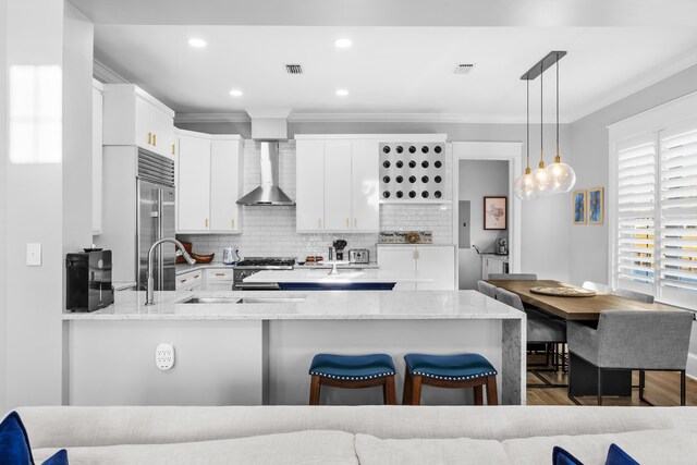 kitchen with white cabinets, high end appliances, pendant lighting, wood-type flooring, and wall chimney range hood