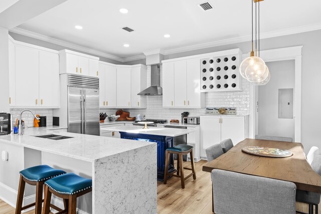 kitchen with pendant lighting, a breakfast bar, white cabinets, wall chimney exhaust hood, and built in fridge