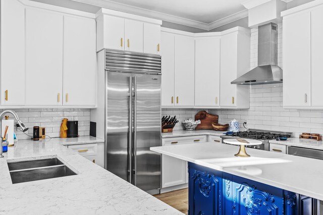 kitchen with light stone counters, white cabinets, wall chimney exhaust hood, stainless steel appliances, and sink