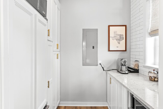 kitchen with decorative backsplash, white cabinetry, light stone counters, light hardwood / wood-style flooring, and electric panel