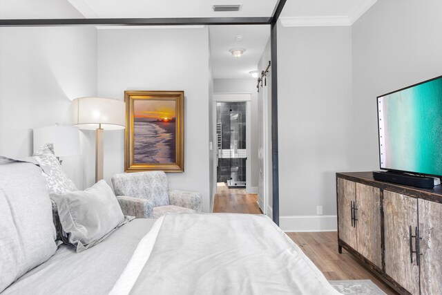 bedroom with a barn door, crown molding, and light hardwood / wood-style floors