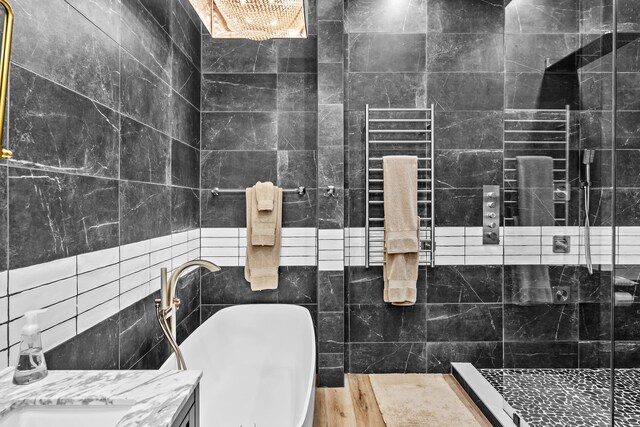 bathroom with a shower, tile walls, vanity, radiator, and hardwood / wood-style flooring