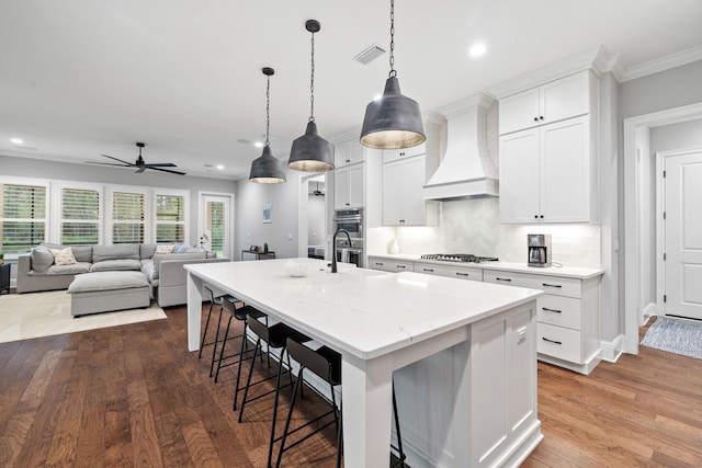 kitchen with white cabinetry, ceiling fan, custom range hood, and a kitchen island with sink