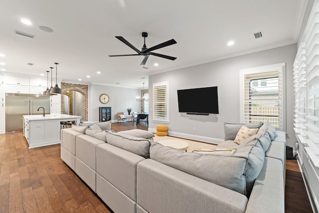 living room with ornamental molding, wood-type flooring, ceiling fan with notable chandelier, and sink