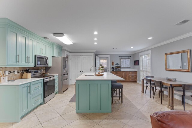 kitchen with light tile patterned floors, crown molding, appliances with stainless steel finishes, an island with sink, and a kitchen breakfast bar