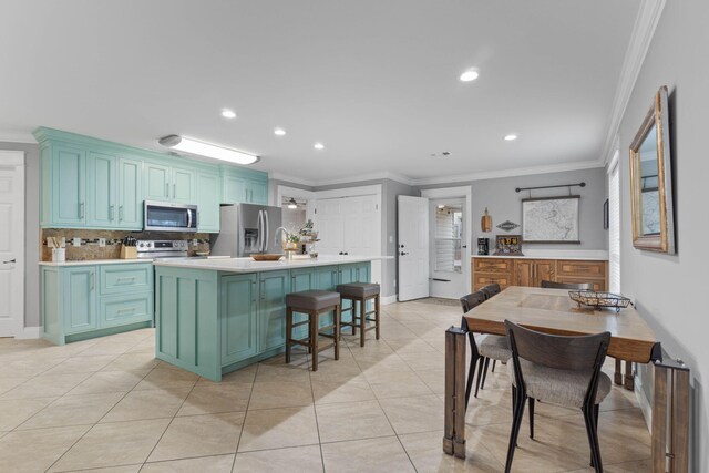 kitchen featuring a kitchen island with sink, a breakfast bar, stainless steel appliances, ornamental molding, and light tile patterned flooring