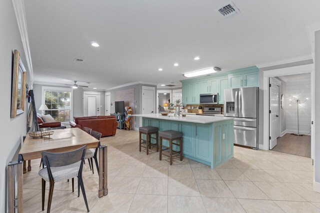 kitchen featuring crown molding, stainless steel appliances, ceiling fan, an island with sink, and a breakfast bar area