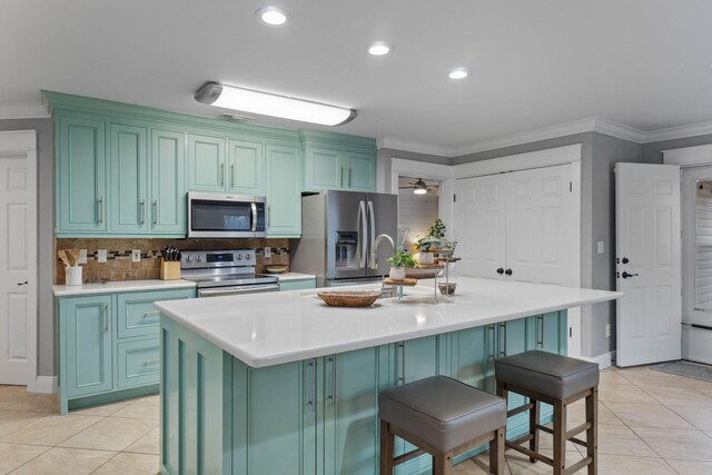 kitchen featuring ceiling fan, light tile patterned floors, stainless steel appliances, and a kitchen island with sink