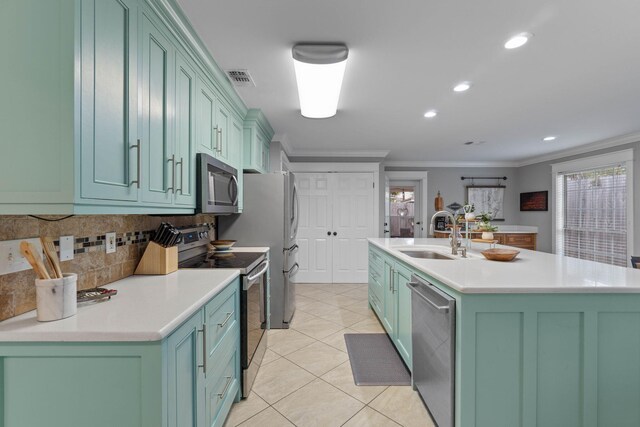 kitchen with light tile patterned floors, crown molding, stainless steel appliances, sink, and a kitchen island with sink