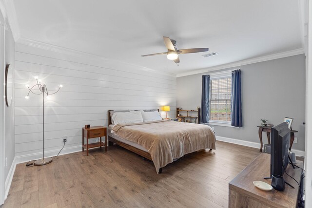 bedroom with wood walls, ceiling fan with notable chandelier, hardwood / wood-style flooring, and crown molding