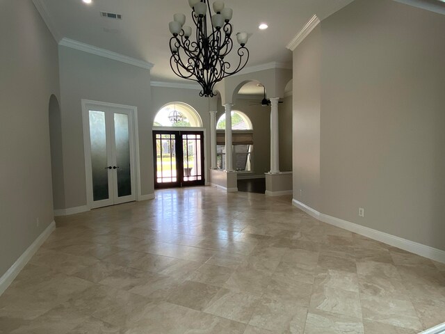 empty room featuring decorative columns, french doors, a chandelier, and ornamental molding