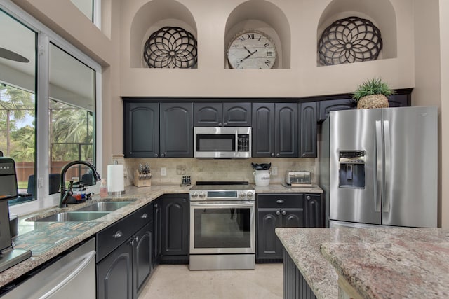 kitchen with light stone counters, sink, a high ceiling, and appliances with stainless steel finishes