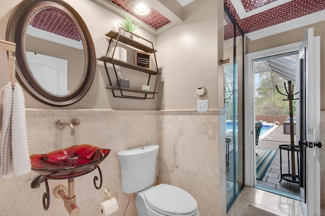 bathroom featuring a skylight, tile patterned floors, crown molding, tile walls, and toilet