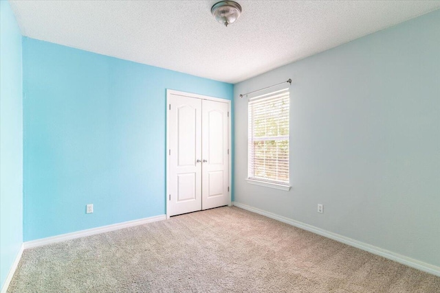 unfurnished bedroom featuring light colored carpet, a textured ceiling, and a closet