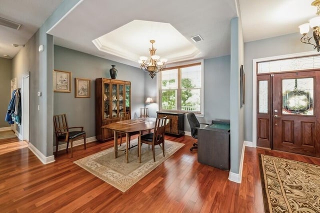 dining room featuring an inviting chandelier, a raised ceiling, and dark hardwood / wood-style flooring