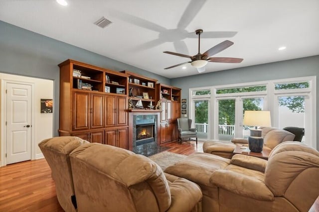 living room featuring french doors, light hardwood / wood-style floors, a premium fireplace, and ceiling fan