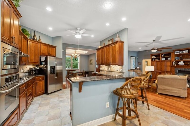 kitchen with tasteful backsplash, kitchen peninsula, stainless steel appliances, dark stone counters, and a breakfast bar area