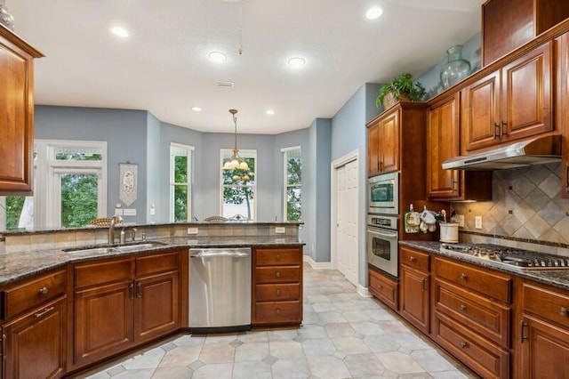 kitchen with appliances with stainless steel finishes, sink, dark stone counters, and decorative light fixtures