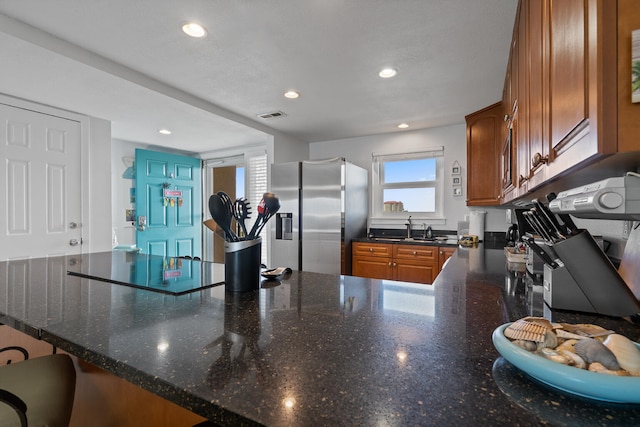 kitchen with stainless steel refrigerator with ice dispenser, dark stone counters, kitchen peninsula, and sink