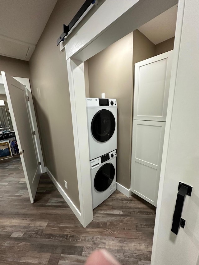 clothes washing area featuring a barn door, stacked washer and clothes dryer, and dark hardwood / wood-style floors