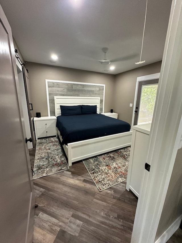 bedroom with dark wood-type flooring, a barn door, and ceiling fan