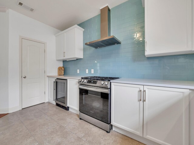 kitchen with decorative backsplash, wine cooler, white cabinets, wall chimney exhaust hood, and stainless steel range