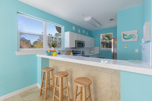 kitchen featuring tile counters, stainless steel appliances, a kitchen bar, light tile patterned floors, and white cabinets