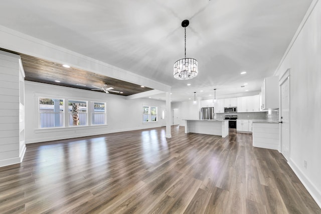 unfurnished living room featuring ceiling fan with notable chandelier and dark wood-type flooring