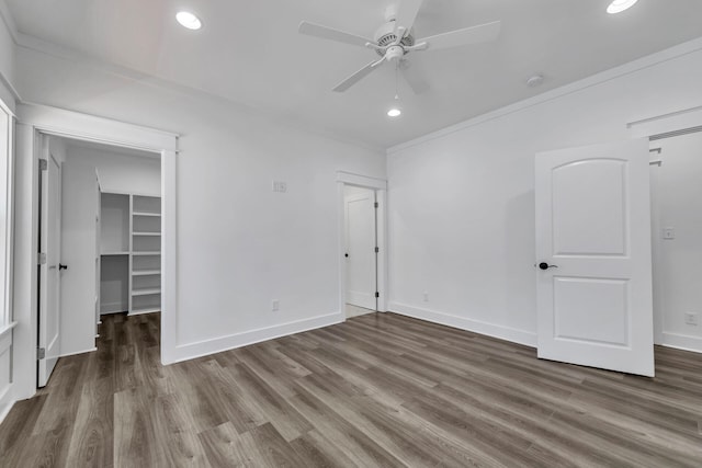 unfurnished bedroom featuring a walk in closet, ornamental molding, a closet, ceiling fan, and hardwood / wood-style floors