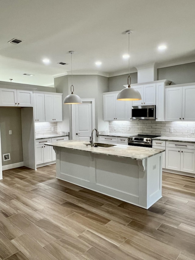 kitchen with a kitchen island with sink, sink, pendant lighting, and stainless steel appliances