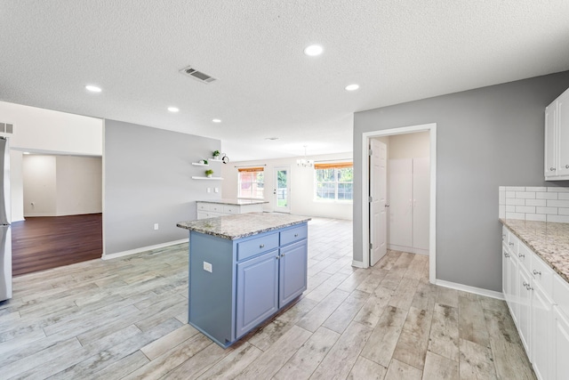 kitchen with white cabinetry, light stone countertops, blue cabinets, a kitchen island, and light wood-type flooring