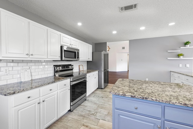 kitchen with a textured ceiling, stainless steel appliances, white cabinetry, and light stone counters