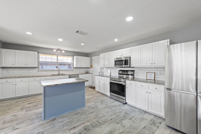 kitchen featuring white cabinets, a kitchen island, appliances with stainless steel finishes, and light hardwood / wood-style flooring