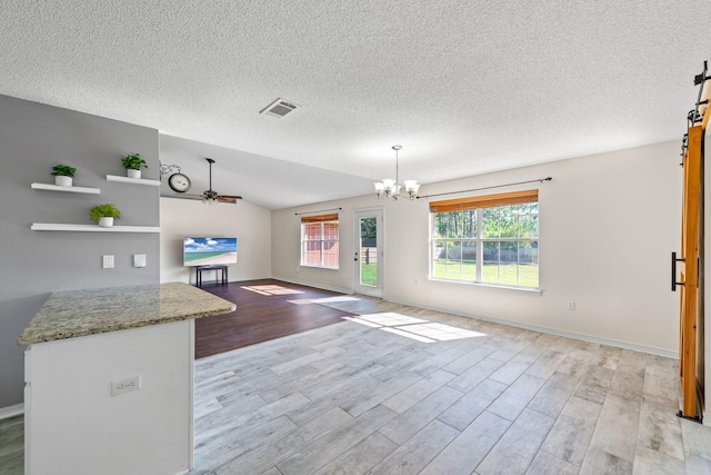 unfurnished living room featuring ceiling fan with notable chandelier, light wood-type flooring, a textured ceiling, and vaulted ceiling