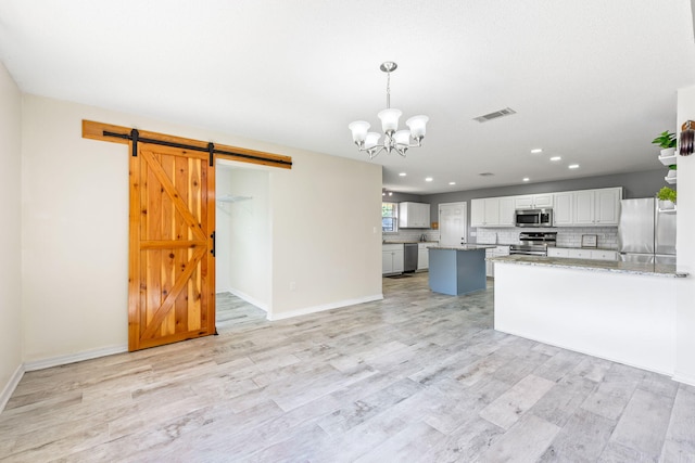 kitchen featuring appliances with stainless steel finishes, pendant lighting, a barn door, light hardwood / wood-style flooring, and white cabinetry