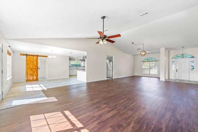 unfurnished living room featuring hardwood / wood-style floors, ceiling fan, a barn door, and vaulted ceiling