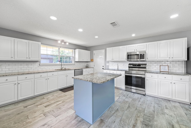 kitchen with sink, light wood-type flooring, appliances with stainless steel finishes, a kitchen island, and white cabinetry